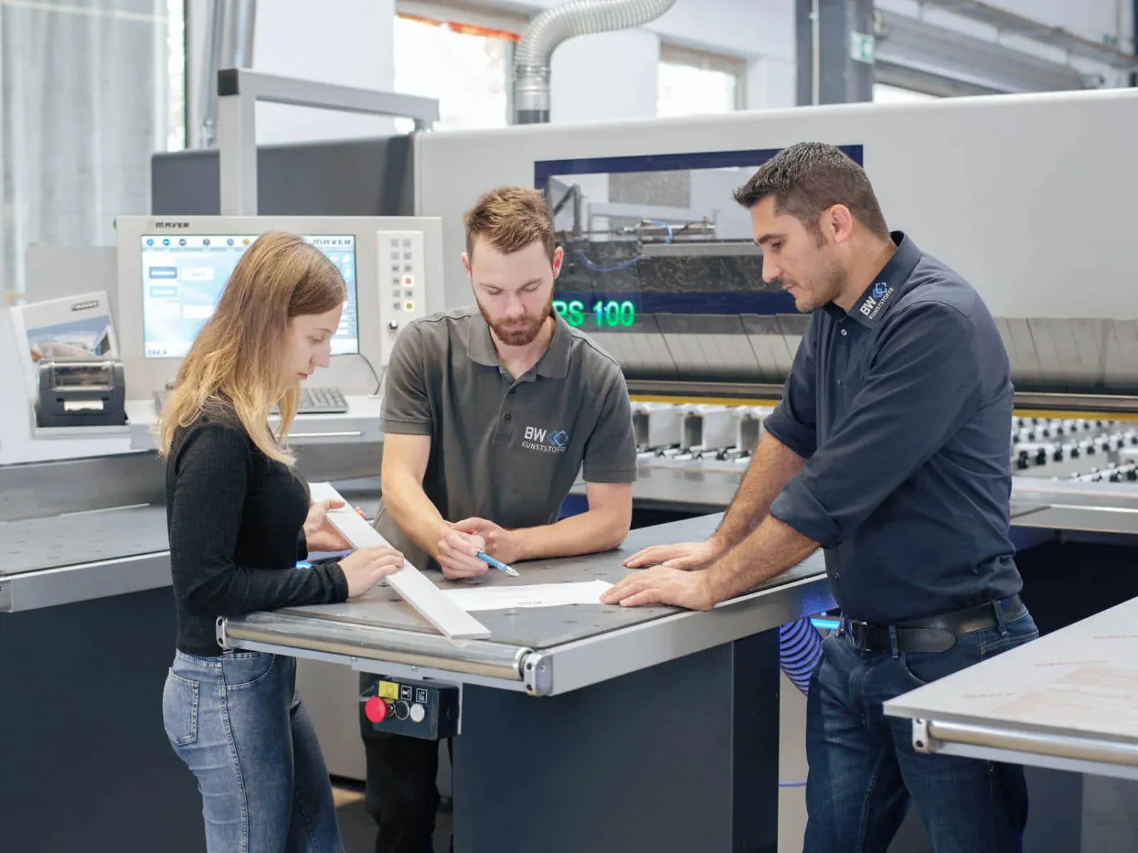 Three Martan employees discuss a plastic part at the machine